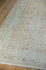 Distressed Oushak carpet's faded apricot, teal vinery pattern with visible worn pile and fringe.
