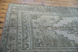 Distressed Oushak rug corner, faded gray, seafoam geometric border, and exposed knot heads.