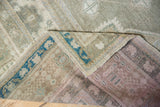 Distressed Oushak rug corner showing worn gray-green pile, blue border, and hand-knotted foundation.