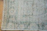 Detail of distressed vintage Oushak rug, showing wear, faded beige, and sage green pattern.