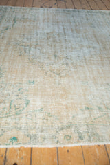 Distressed vintage Oushak carpet pile texture in faded beige and subtle green tones.