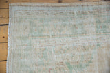 Distressed Oushak carpet's edge, showing faded seafoam green, peach tones, and exposed knot heads.