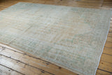 Distressed Oushak rug corner with faded seafoam green motifs and fringed edge.