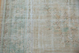 Faded peach and seafoam green hues on the distressed Oushak carpet's worn texture.