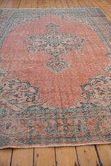 Distressed vintage Oushak rug end, showing pale blush field, aqua border, and short fringe.