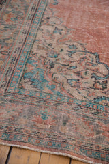 Distressed vintage Oushak rug close-up: worn pale blush field, mint and aqua motifs, foundation visible.