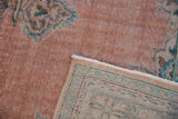Distressed Oushak rug corner revealing pale blush pile, foundation showing, and aqua patterned reverse.