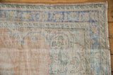 Distressed Oushak rug corner showing worn blush pile, pale blue border, and fringe.