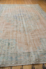 Distressed Turkish Oushak carpet detail: faded blush, blue floral motifs, and visible wear.