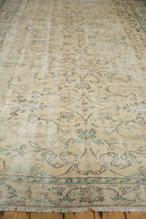 Distressed vintage Oushak rug, angled view revealing even wear, green vinery, and fringe.