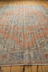 Distressed Oushak rug with worn pile, visible foundation, and muted terracotta and blue floral motifs.