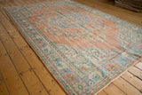Distressed corner of vintage Oushak carpet, showing foundation, pale terracotta, blue, green floral motifs and fringe.