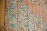 Distressed Oushak rug edge featuring worn terracotta, denim blue, and ivory floral motifs.
