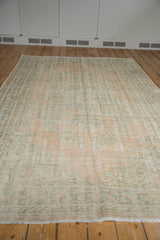 Distressed vintage Oushak carpet with soft apricot field and faded mint green floral patterns.
