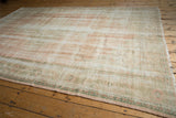 Vintage distressed Oushak rug's faded rose, ivory, green hues, worn texture, and intact fringe.