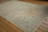 Distressed Oushak carpet with worn pile showing soft floral patterns in faded teal.