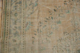 Distressed Oushak rug texture showing worn beige pile, faded mint green, and exposed foundation.