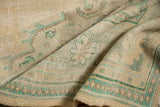 Worn beige pile with sea foam green geometric patterns on a folded vintage Oushak rug.
