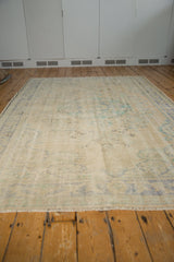 Distressed ivory field with faded blue and green floral motifs on a vintage Oushak rug.