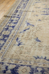 Distressed Oushak carpet pile, faded ivory field, pale coffee tones, and cobalt border.