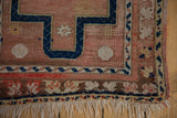 Distressed Anatolian rug showing navy hook and latch motif, dusty rose field, and worn fringe.