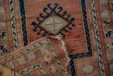 Folded corner of distressed Anatolian rug reveals worn pile, navy gul, and frayed fringe.