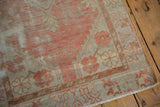 Distressed corner of an Oushak rug, showcasing faded red florals, ivory ground, and intact selvage.