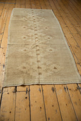 Distressed beige Oushak runner end, showing its texture, intact selvage, and geometric motifs.