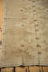 Vintage distressed Oushak rug's textured ivory pile, geometric motif, and side selvage.
