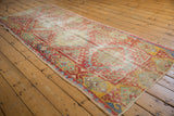 Distressed pile of a vintage Oushak runner, revealing areas of foundation with cherry red and mint green motifs.