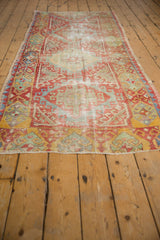 Distressed Oushak rug corner, worn geometric motifs in red, saffron, mint, and blue.