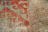 Distressed Oushak rug close-up: worn red and green geometric pile, exposed foundation, and striped back.