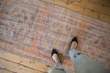 Distressed vintage Oushak runner in faded terracotta, blue, and mint green, shown with feet.