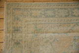 Fringed edge and worn knot heads of the distressed Oushak rug in faded apricot and green.