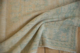 Distressed Oushak rug pile with mostly even wear, faint blossoming vinery in muted apricot and green.