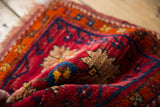 Folded vintage Oushak rug with cherry red, tangerine, and sapphire blue serrated floral motifs.