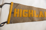 Close view of hand-sewn yellow block letters and dark felt ties on the Highland pennant.