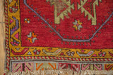 Vintage Oushak rug corner showing vibrant red field, saffron border, geometric patterns, and tattered fringe.