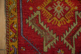 Vintage Oushak rug close-up: saffron vine border, red field, threadbare pile, tattered edge.