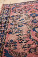 Vintage Lilihan rug's pale raspberry field, intricate blue scrolling leaf motifs, and wear.