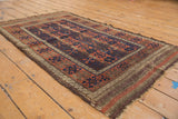 Antique Persian Belouch rug showing germinating plant columns, madder root, navy blue, and aged texture.
