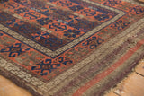 Antique Belouch rug's geometric border in madder root, navy, and chestnut, with a tattered end.