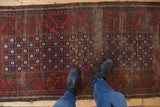 Antique Belouch runner with significant pile wear, madder red, and navy pomegranate motifs.