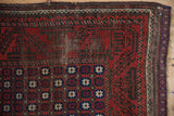Repeating madder root and navy paneled starburst motifs on an antique Belouch rug, showing foundation wear.