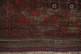 Antique Belouch rug corner, deep red meandering vine border, navy band, and visible foundation.