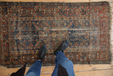 Antique Malayer rug, worn navy blue Herati pattern, madder root, exposed foundation, and black boots.
