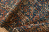 Antique Malayer rug close-up: Herati field motif, meandering border, madder root, navy, and visible wear.