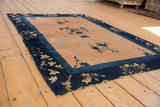 Antique Chinese Peking rug detail: ornate dark blue border, sprawling vines, pale peach field, visible foundation.