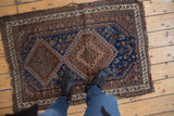 Afshar rug close-up displaying indigo field, geometric floral blossoms, and tattered edge.