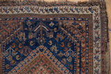 Corner of an Antique Afshar rug featuring indigo, chestnut, ivory tribal geometric patterns and aged fringe.